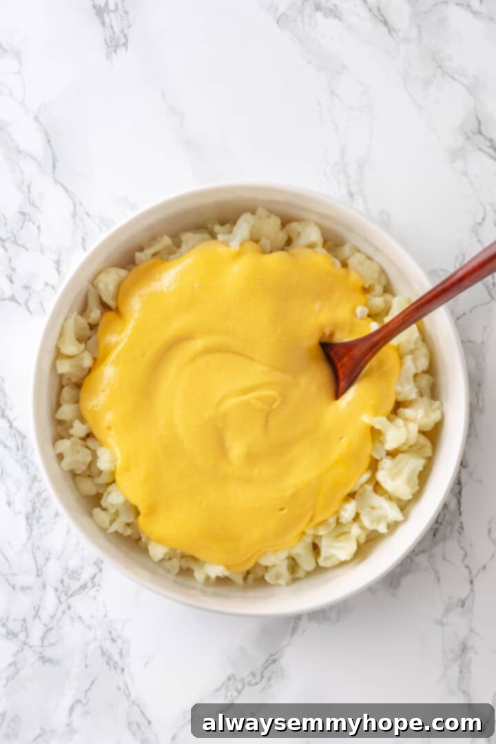 Rich vegan cheese sauce being poured generously over a bowl of cooked cauliflower florets.