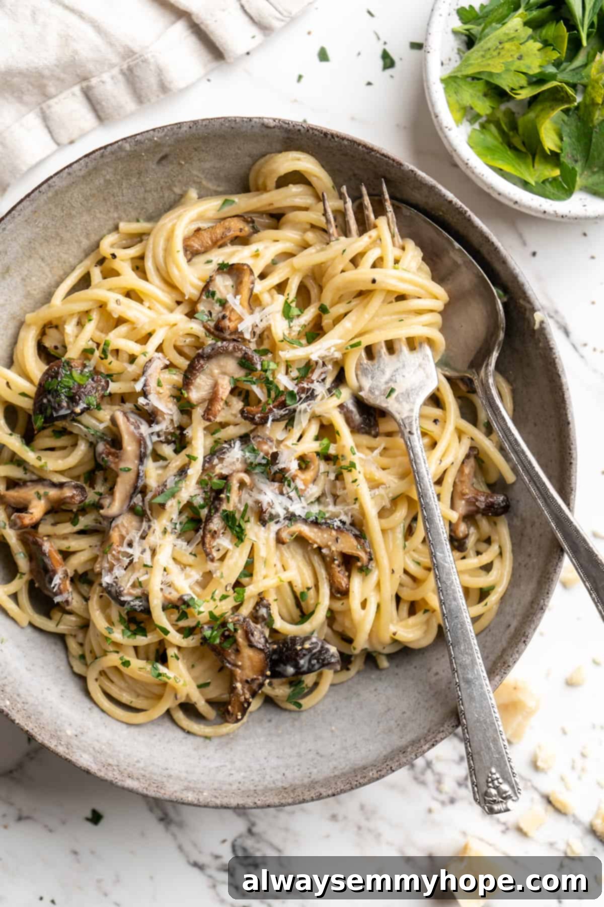 Overhead view of miso butter pasta on plate with fork and spoon, garnished with fresh parsley.