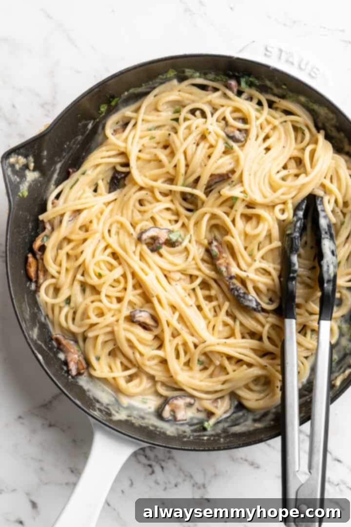 Overhead view of miso butter pasta in skillet with tongs, being tossed to coat evenly with the rich sauce.