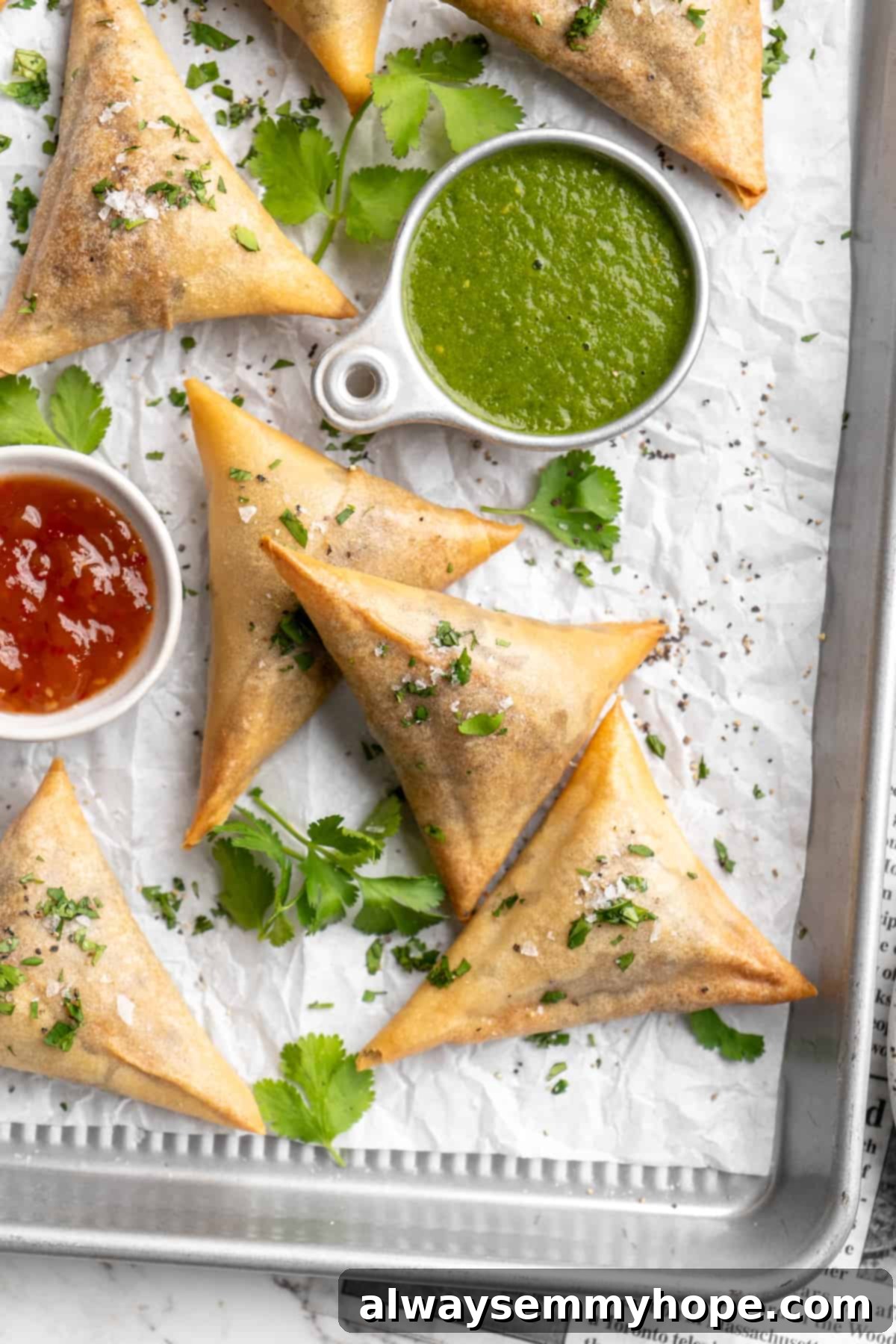 Overhead view of sambusas on parchment-lined baking sheet with dipping sauces