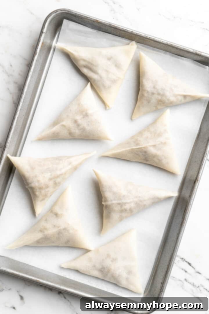 Overhead view of uncooked sambusas on parchment-lined baking sheet