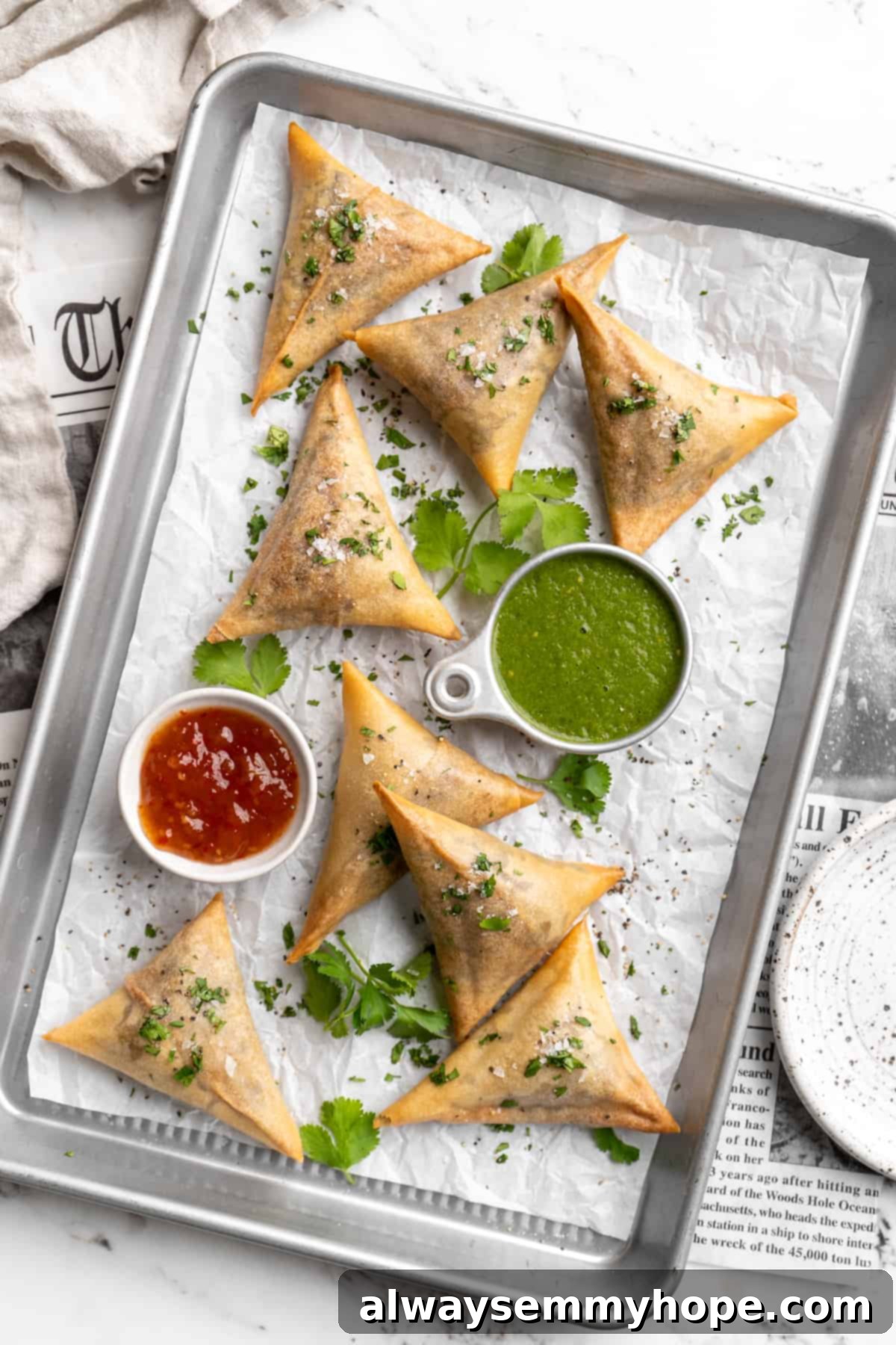 Overhead view of sambusas on parchment-lined baking sheet with dipping sauces
