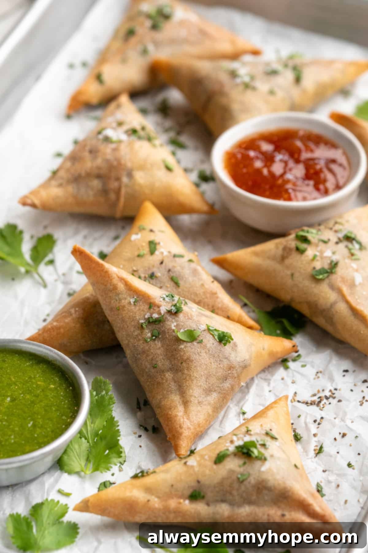 Vegan sambusas on parchment-lined baking sheet with dipping sauces