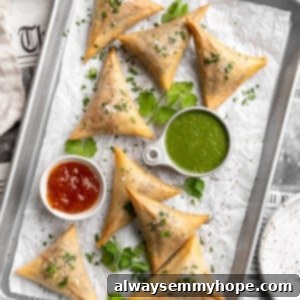 Overhead view of sambusas on parchment-lined baking sheet with dipping sauces
