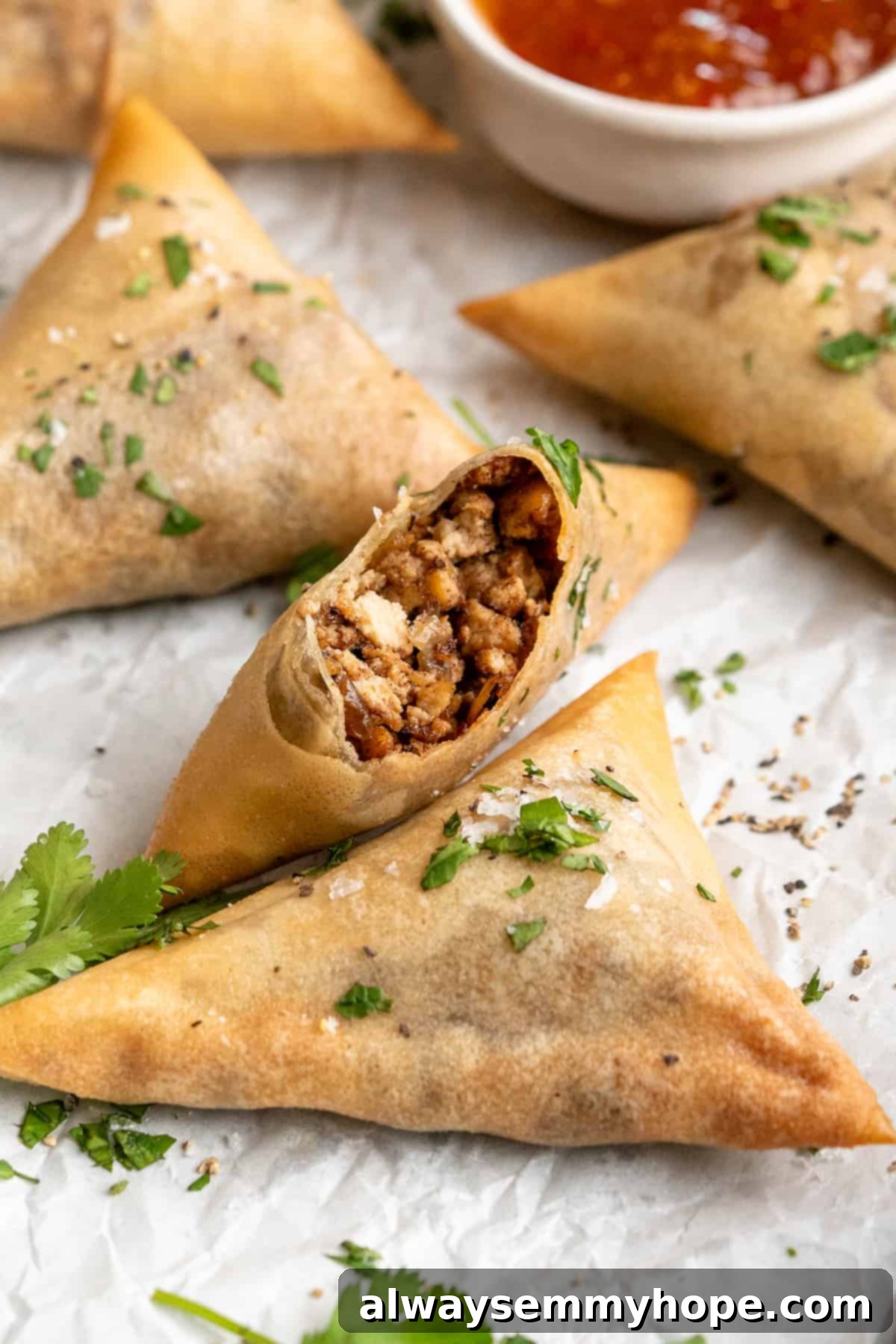 Sambusas on parchment paper, with one bitten to show filling inside