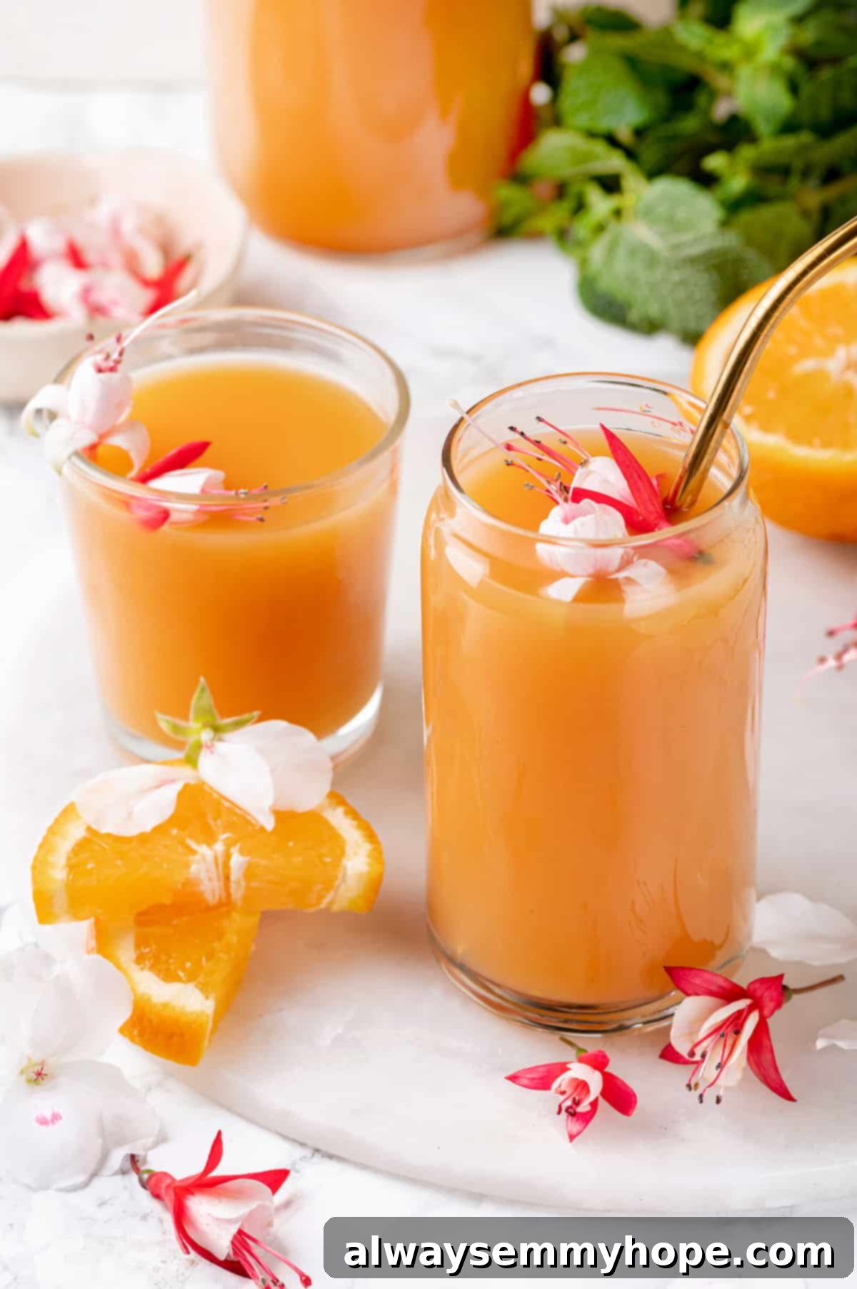 Two glasses of POG juice, one with a straw, and tropical flowers for garnish