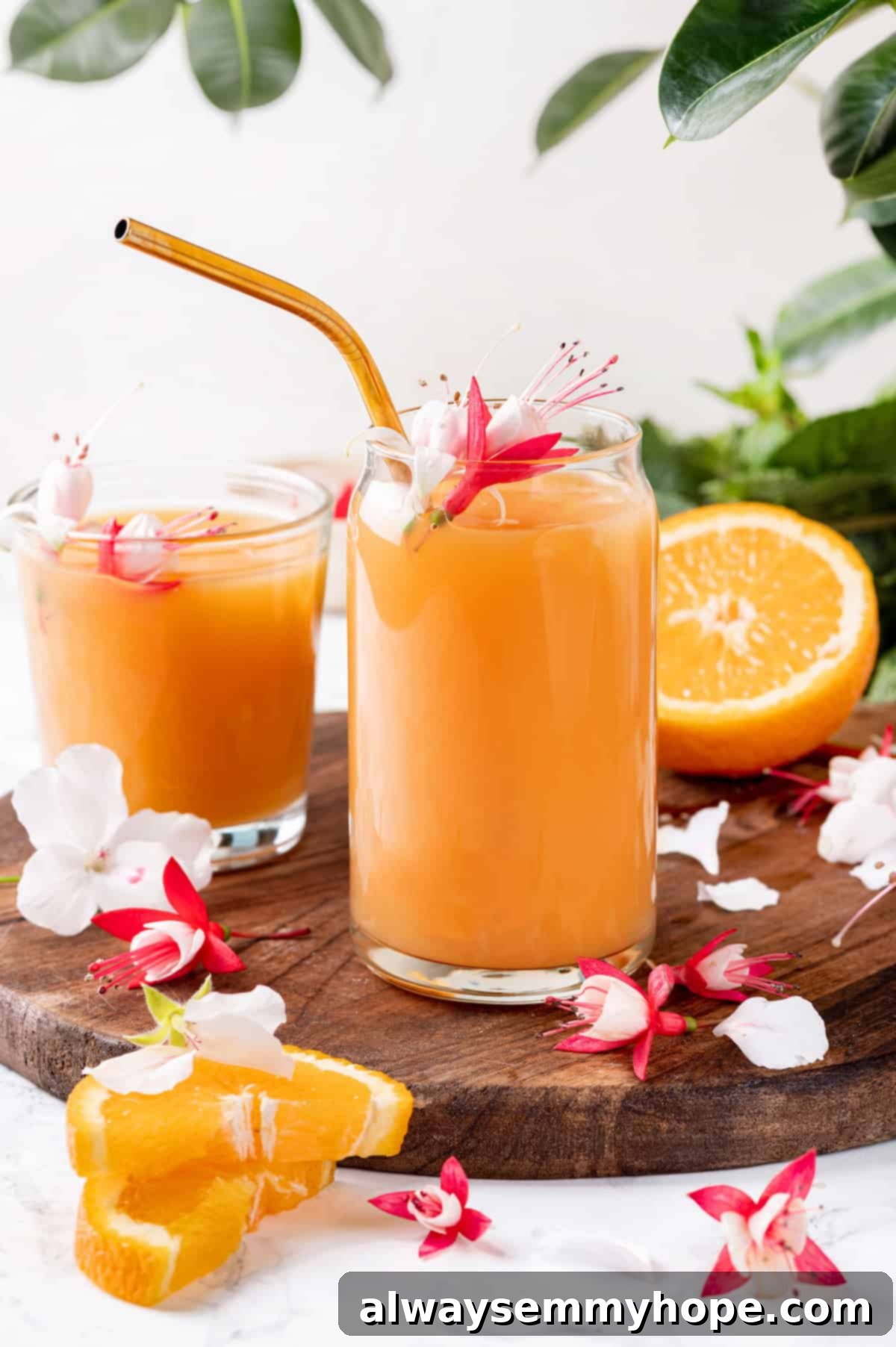 Two glasses of POG juice on wooden board with sliced oranges and tropical flowers