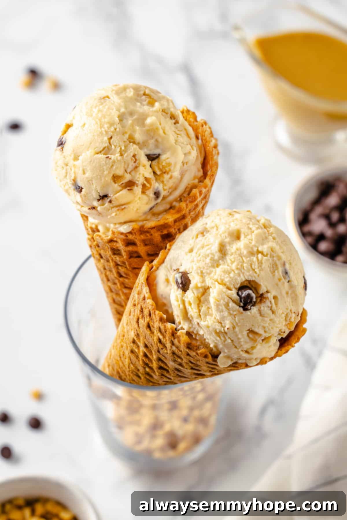 Two waffle cones brimming with luxurious no-churn peanut butter ice cream, topped with extra chopped peanuts and chocolate shavings.