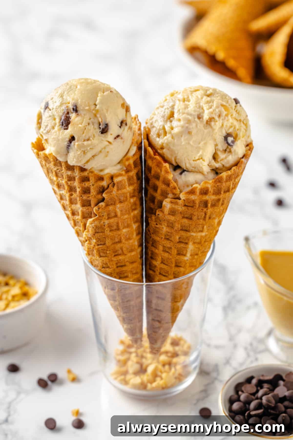 Two waffle cones filled with generous scoops of no-churn vegan peanut butter ice cream, standing upright in a glass.