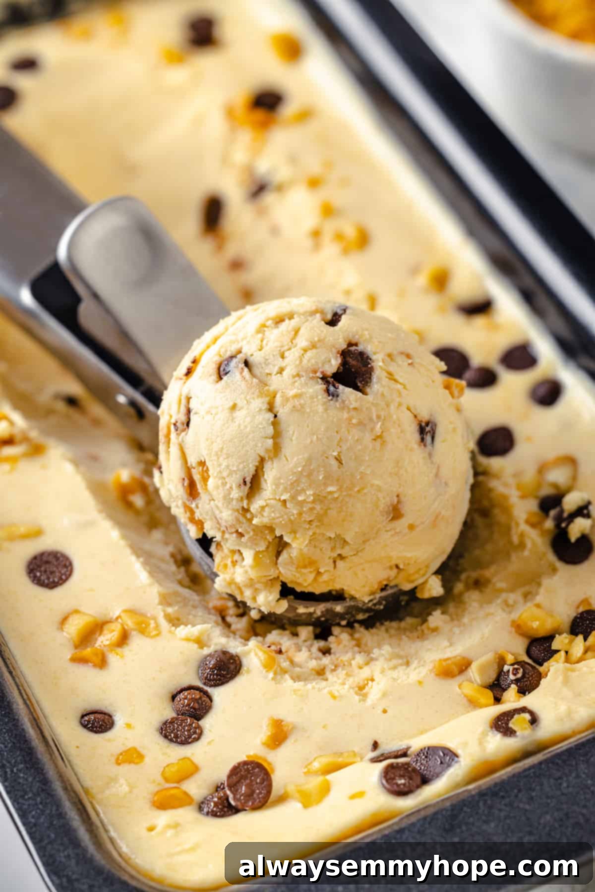 A scoop of rich peanut butter ice cream being lifted from a loaf pan, showcasing its smooth and creamy texture.