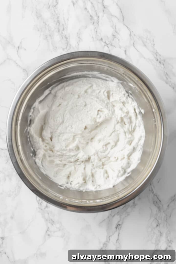 An overhead view of beautifully whipped coconut cream in a glass mixing bowl, ready for the next steps.