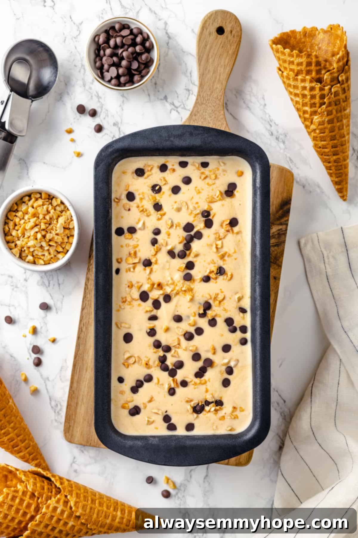 A close-up overhead view of the perfectly set no-churn peanut butter ice cream in a loaf pan, garnished with peanuts and chocolate chips.