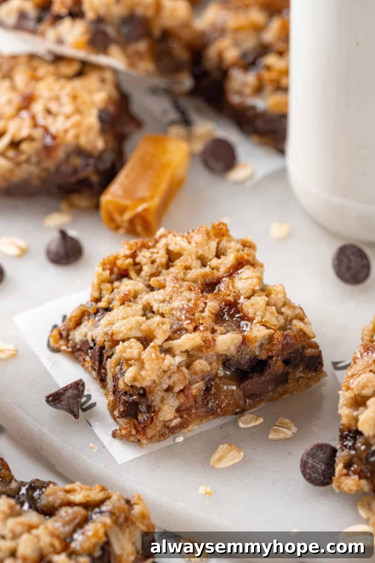 Close-up of a Vegan Carmelita Bar Single vegan carmelita square on a marble board with more bars blurred in the background, showcasing its delicious layers.