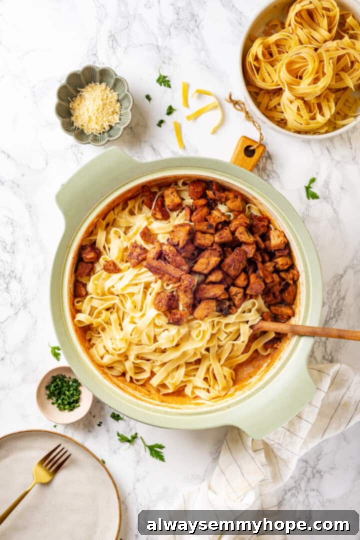 Stirring fettuccine and vegan chicken into the creamy Cajun sauce in a large pan