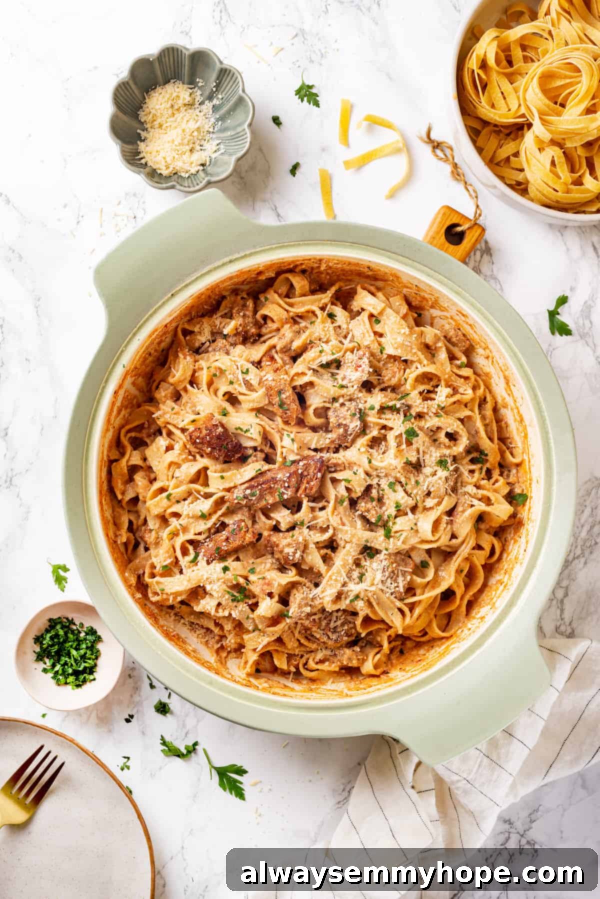 Overhead view of Cajun pasta in pan surrounded by garnishes and a bowl of uncooked fettuccine