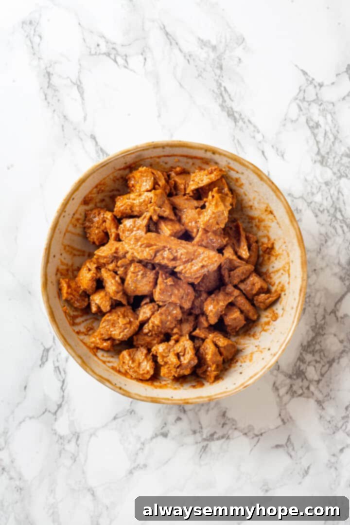 Overhead view of marinated vegan chicken pieces in a bowl, coated evenly with seasoning