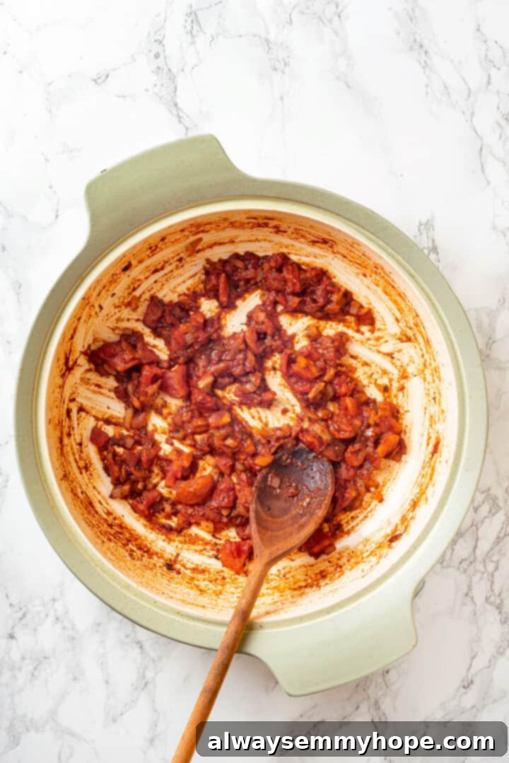 Overhead view of diced tomatoes and tomato paste being added to the sautéed aromatics in a pan