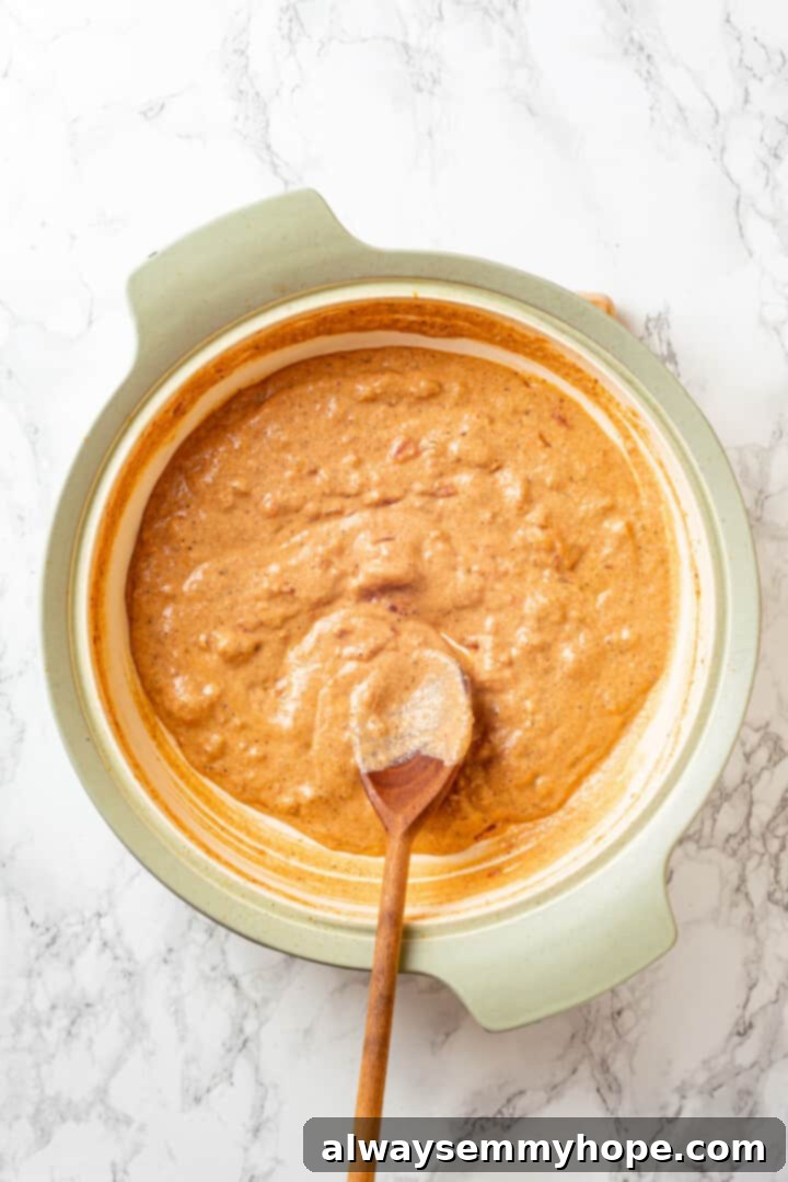 Overhead view of creamy Cajun sauce simmering in a pan with a wooden spoon