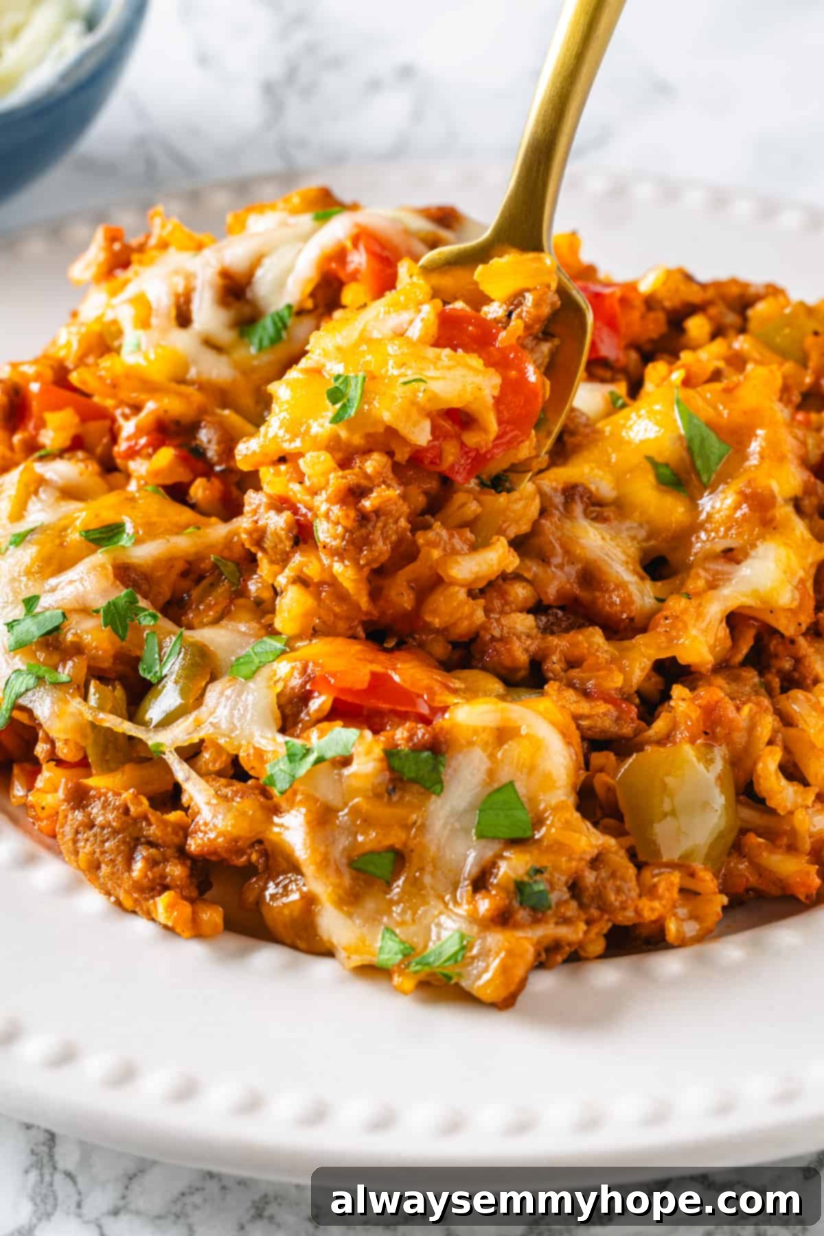 A serving of vegan stuffed pepper casserole in a white bowl with a gold fork. Vegan stuffed pepper casserole in white dish with gold fork