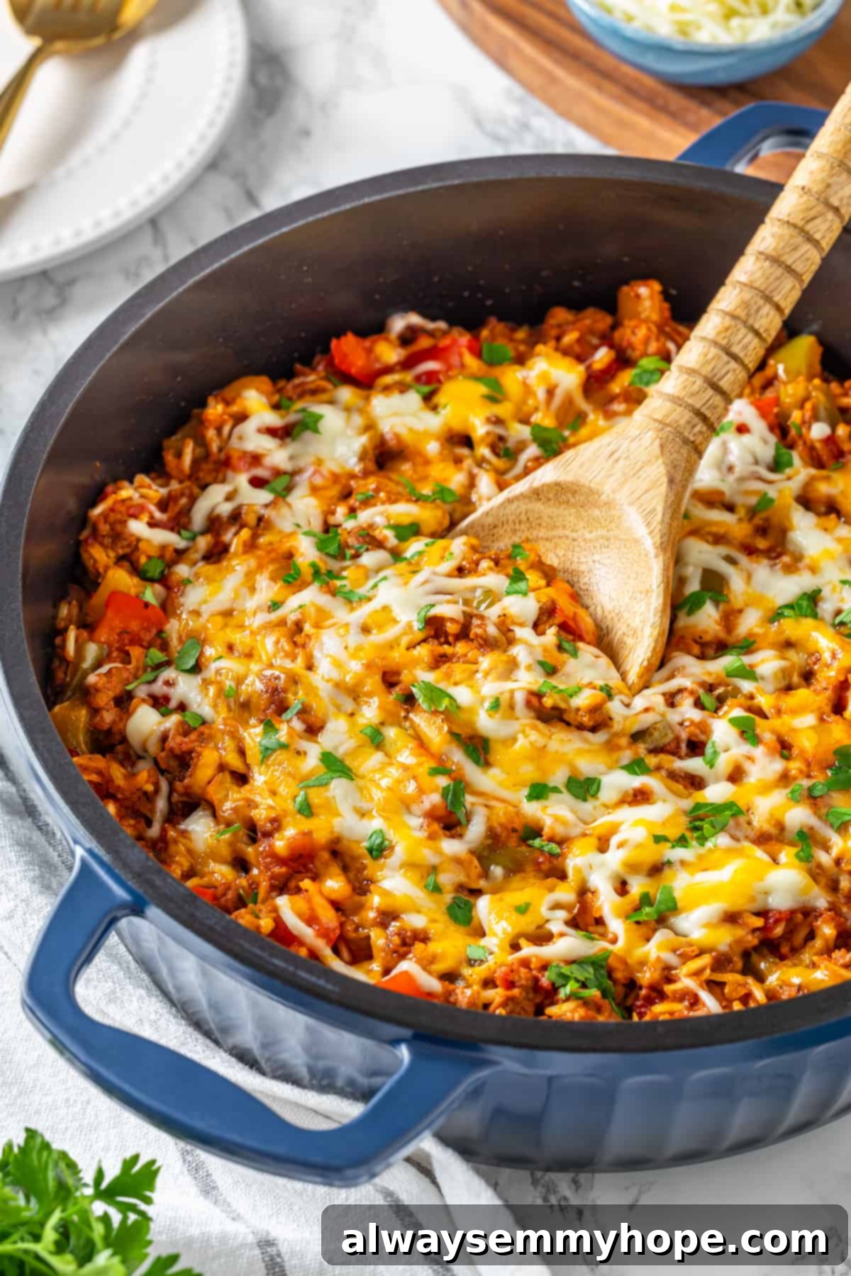 A large skillet filled with vegan stuffed pepper casserole and a wooden spoon. Vegan stuffed pepper casserole simmering in a skillet with a wooden spoon