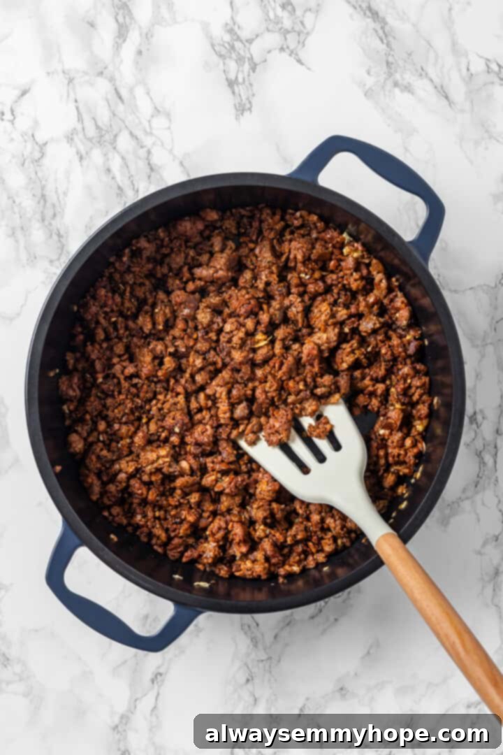 A spatula stirring vegan ground beef in a skillet. Overhead view of vegan ground beef in skillet with spatula