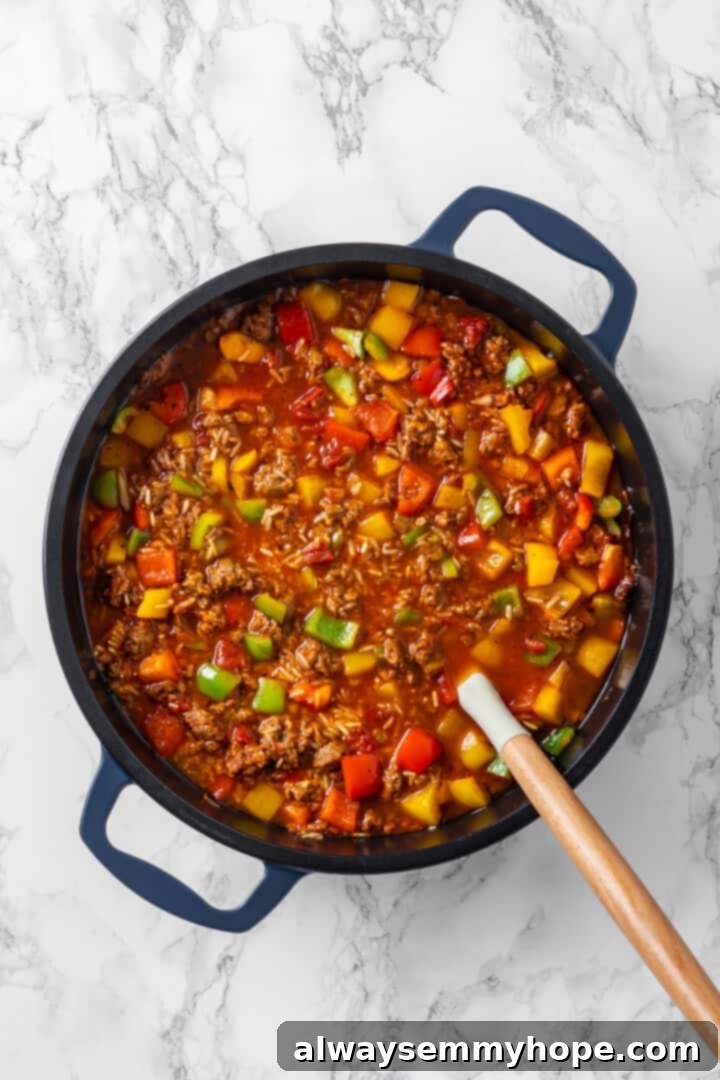 Uncooked brown rice mixed into the casserole base in a skillet. Overhead view of stuffed pepper casserole after adding rice
