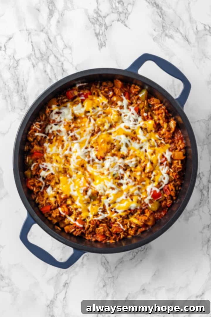 Vegan stuffed pepper casserole in a skillet topped with melted cheese. Overhead view of stuffed pepper casserole in skillet after topping with cheese