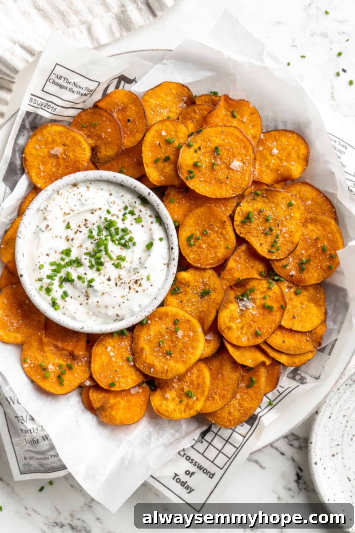 Once you start eating these crispy homemade sweet potato chips, you won’t be able to stop! Super easy to make with only 3 ingredients. Overhead view of crispy sweet potato chips artfully arranged on a plate with a bowl of savory dip