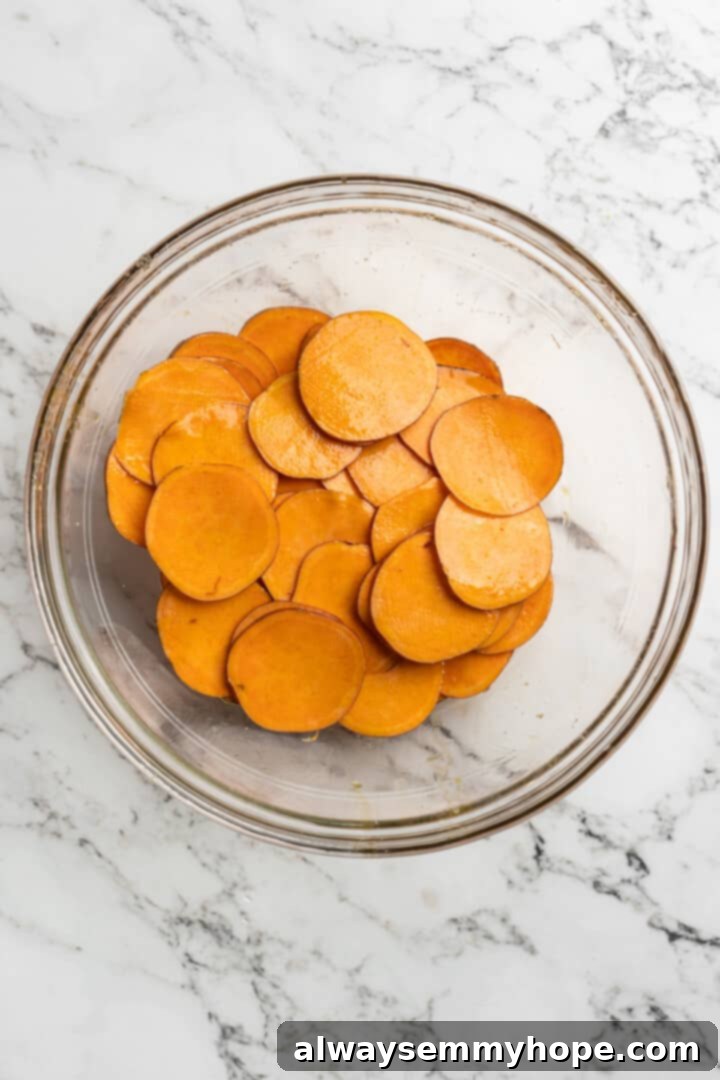 Once you start eating these crispy homemade sweet potato chips, you won’t be able to stop! Super easy to make with only 3 ingredients. Overhead view of sweet potato slices being tossed with olive oil in a bowl
