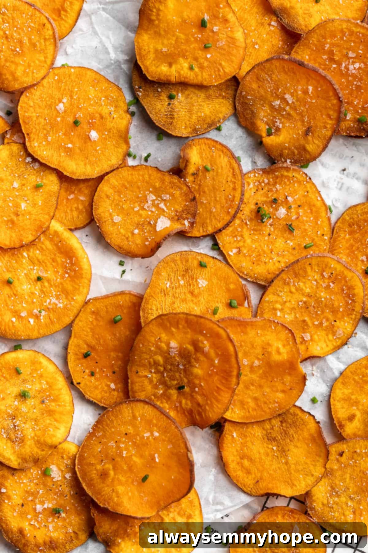 Once you start eating these crispy homemade sweet potato chips, you won’t be able to stop! Super easy to make with only 3 ingredients. Homemade sweet potato chips topped with fresh chives and flaky sea salt, arranged on a rustic plate