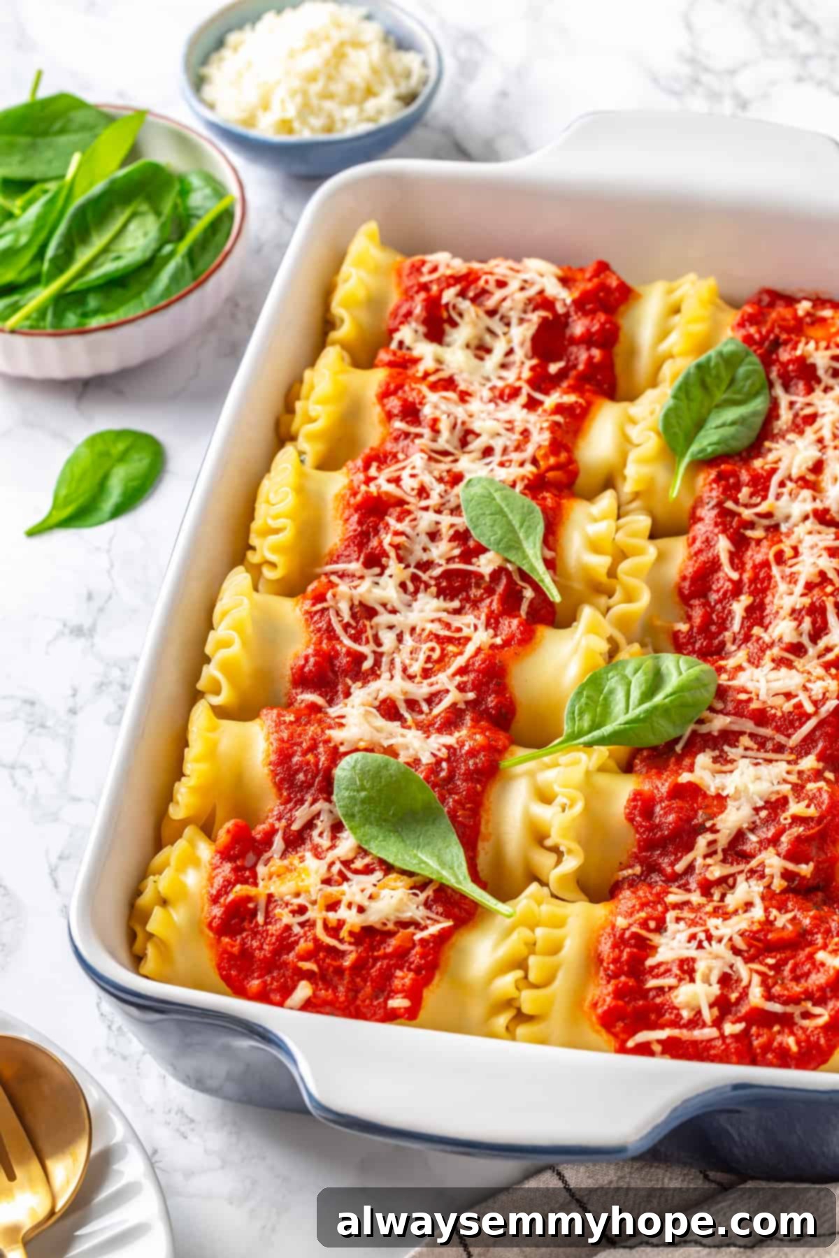 A ceramic blue baking dish filled with perfectly baked vegan spinach ricotta lasagna rolls, topped with fresh basil leaves.