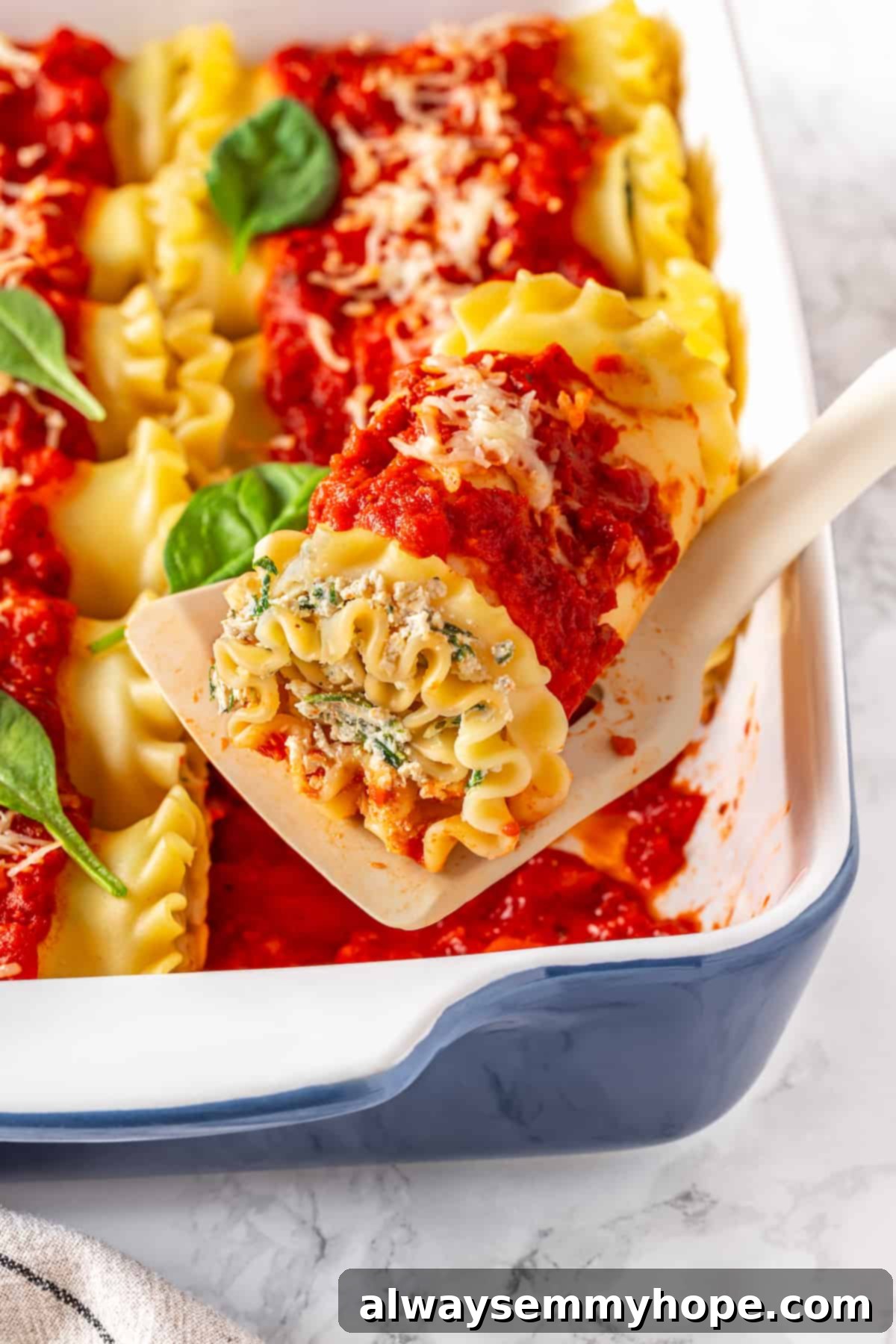 Spatula lifting a single vegan lasagna roll from a casserole dish, showing the perfectly formed spiral.