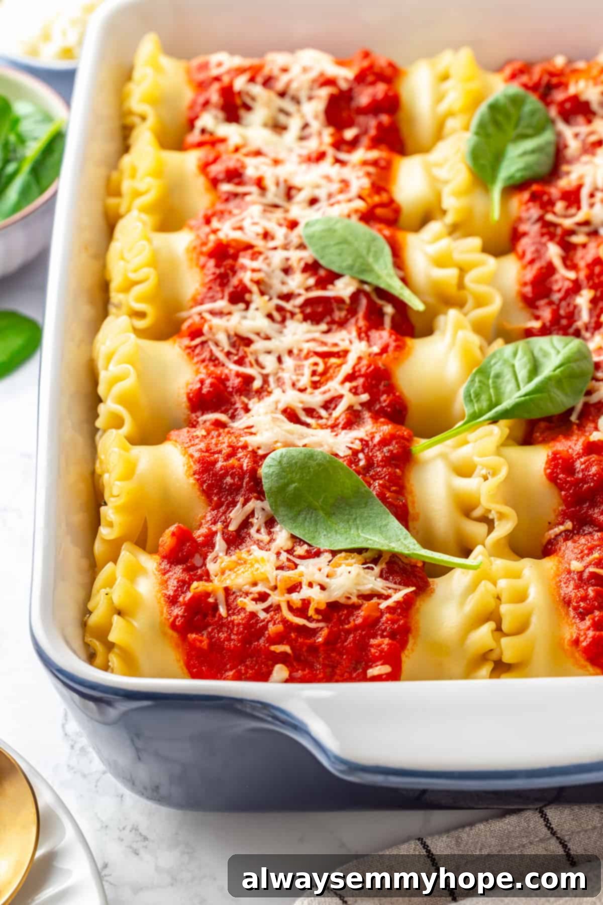 Close-up overhead shot of baked vegan lasagna rolls in a blue ceramic baking dish, garnished with fresh basil leaves.