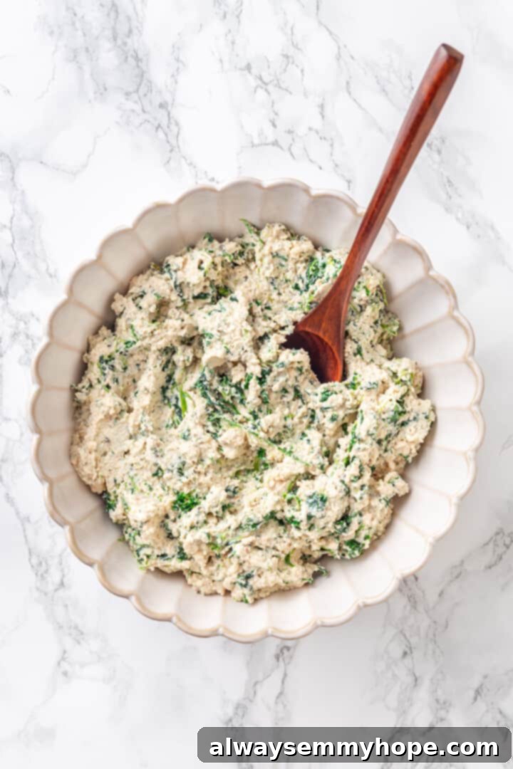 Overhead view of a creamy spinach ricotta filling in a mixing bowl with a wooden spoon.