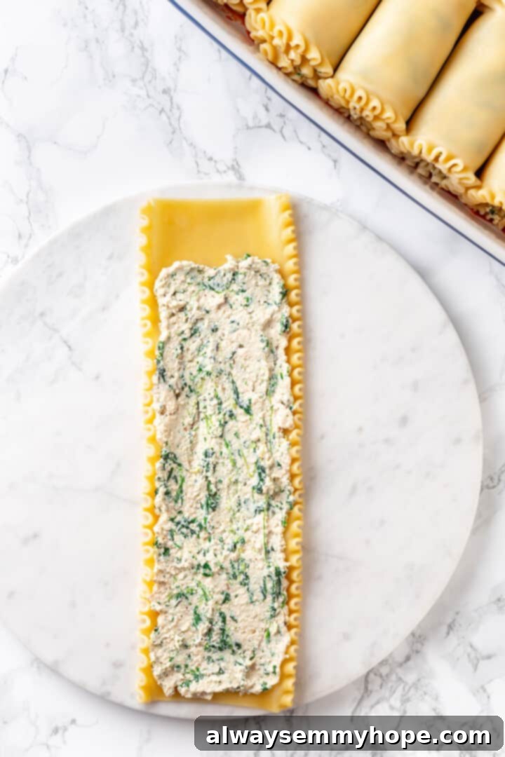 Overhead view of a cooked lasagna noodle with a generous amount of spinach ricotta filling spread evenly over it, ready to be rolled.