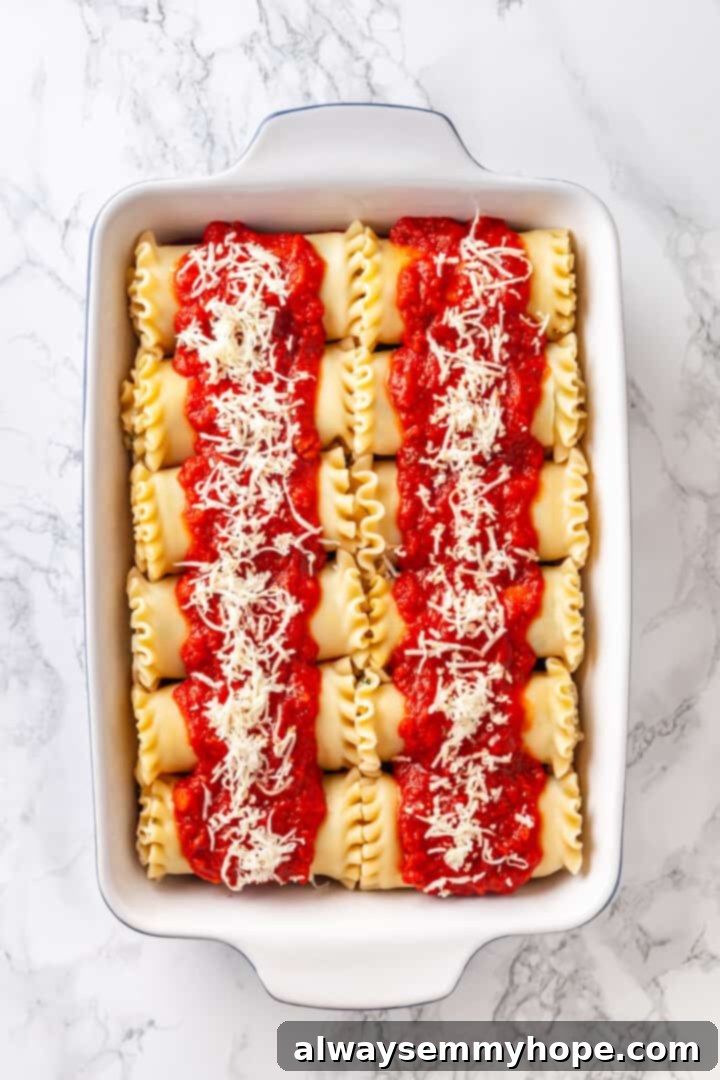 Overhead view of vegan lasagna rolls in a baking dish, generously topped with marinara sauce and vegan mozzarella, ready for the oven.