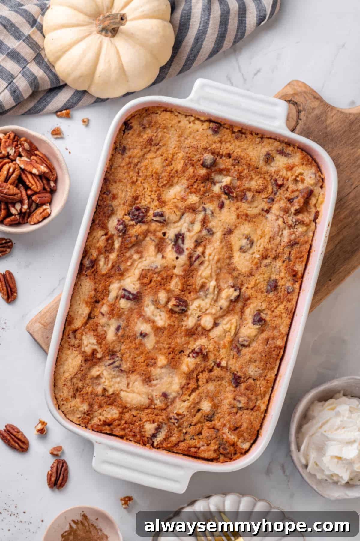 Full of cozy spices, super moist, and studded with toasted pecans, this easy vegan pumpkin dump cake can be whipped up in no time at all! Overhead view of a freshly baked pumpkin dump cake in a white casserole dish, golden brown and inviting.