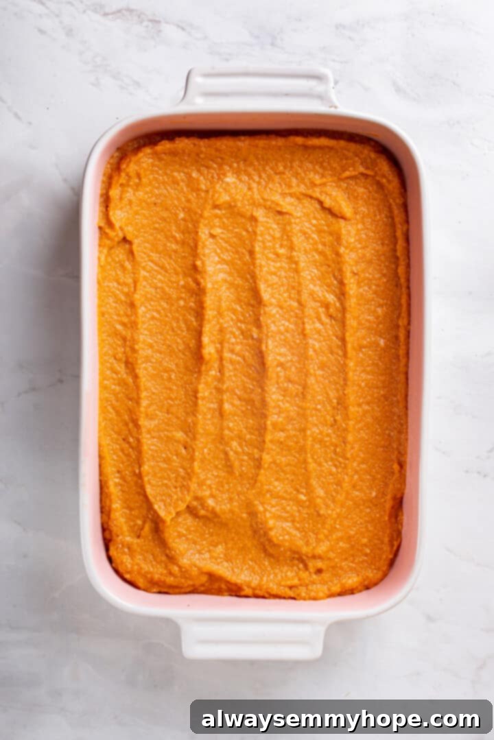 Full of cozy spices, super moist, and studded with toasted pecans, this easy vegan pumpkin dump cake can be whipped up in no time at all! Overhead view of the pumpkin layer evenly spread in a casserole dish, ready for topping.