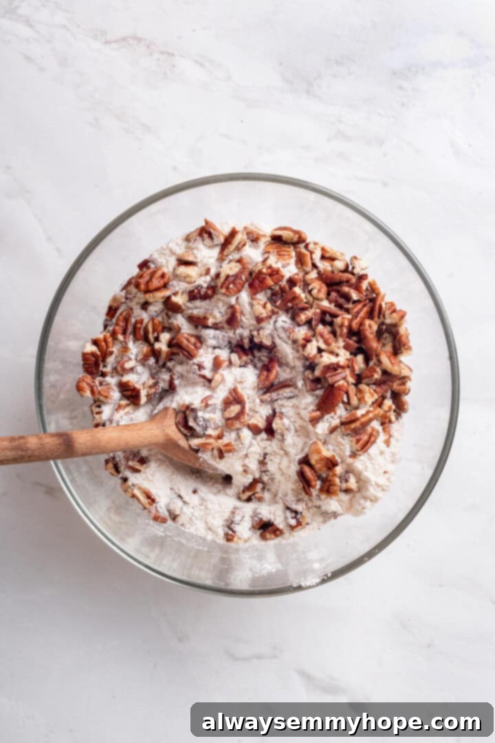 Full of cozy spices, super moist, and studded with toasted pecans, this easy vegan pumpkin dump cake can be whipped up in no time at all! Overhead view of the dry cake mix and chopped pecans mixed in a bowl, ready for topping.