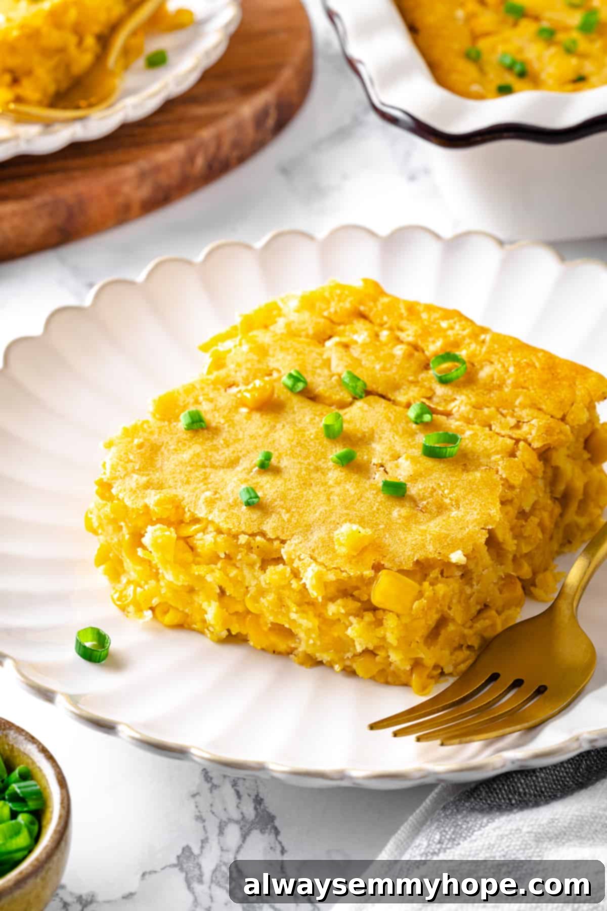 A delicious serving of vegan cornbread pudding on a white plate with a gold fork, showing its golden crust and moist interior.