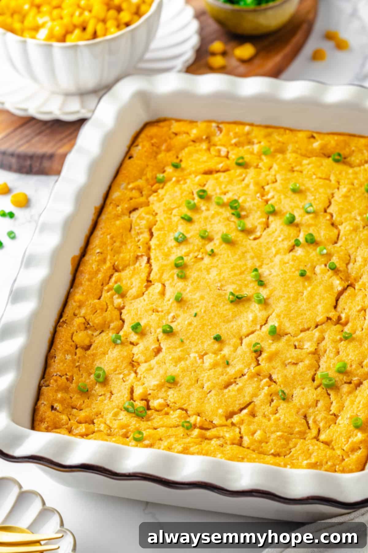 A full white casserole dish of vegan cornbread pudding, freshly baked and garnished with vibrant green onions scattered over the golden-brown top.