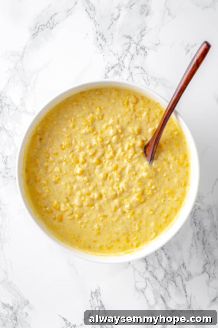 Overhead view of a creamy vegan cornbread pudding mixture in a large mixing bowl with a wooden spoon, ready to be transferred to a baking dish.