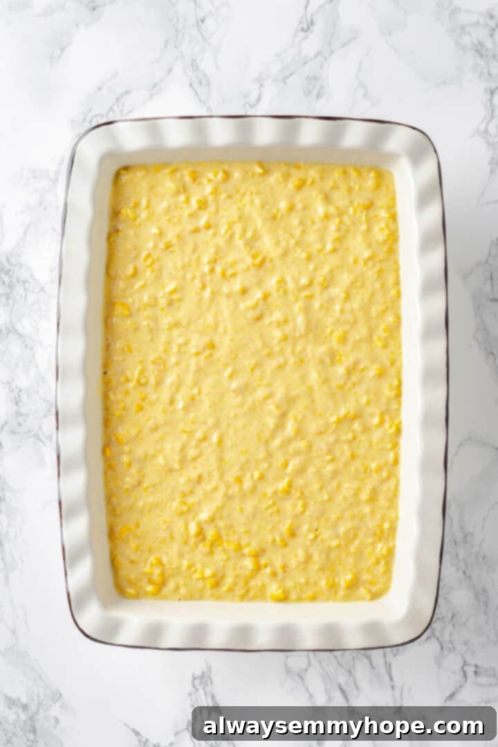 An overhead shot of uncooked vegan cornbread pudding batter evenly spread in a white casserole dish, perfectly prepped for baking.