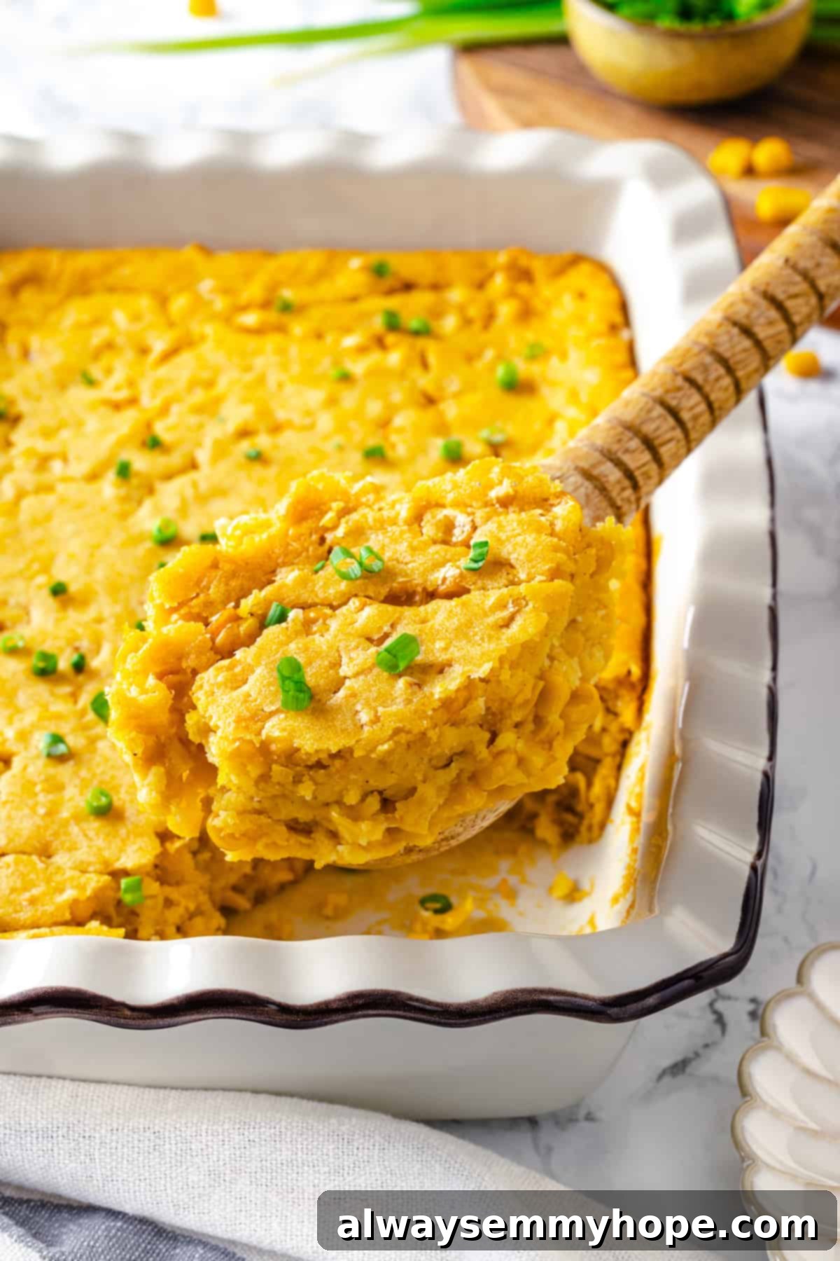 A scoop of warm, moist vegan cornbread pudding being served from a white casserole dish, highlighting its rich texture and appealing golden color.