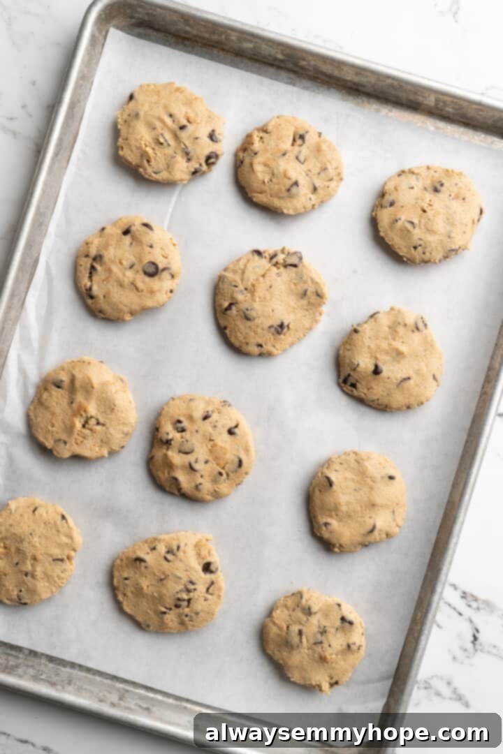 Thick, chewy, and loaded with chocolate, graham crackers, and marshmallows, this one-bowl s'mores cookie recipe is a guaranteed hit! Overhead view of flattened s'mores cookie dough on a baking sheet, creating a base for the marshmallow.