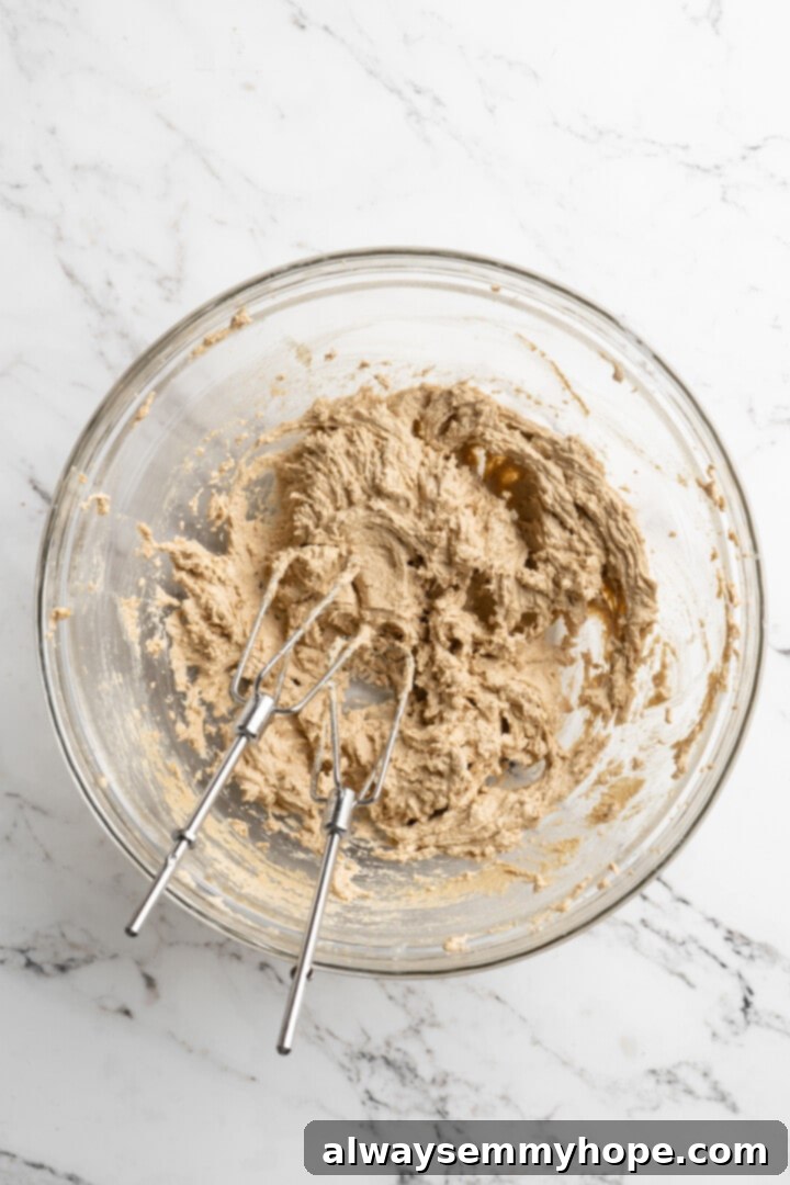 Thick, chewy, and loaded with chocolate, graham crackers, and marshmallows, this one-bowl s'mores cookie recipe is a guaranteed hit! Overhead view of wet ingredients for cookies: softened vegan butter, brown sugar, vegan milk, and vanilla extract in a mixing bowl.