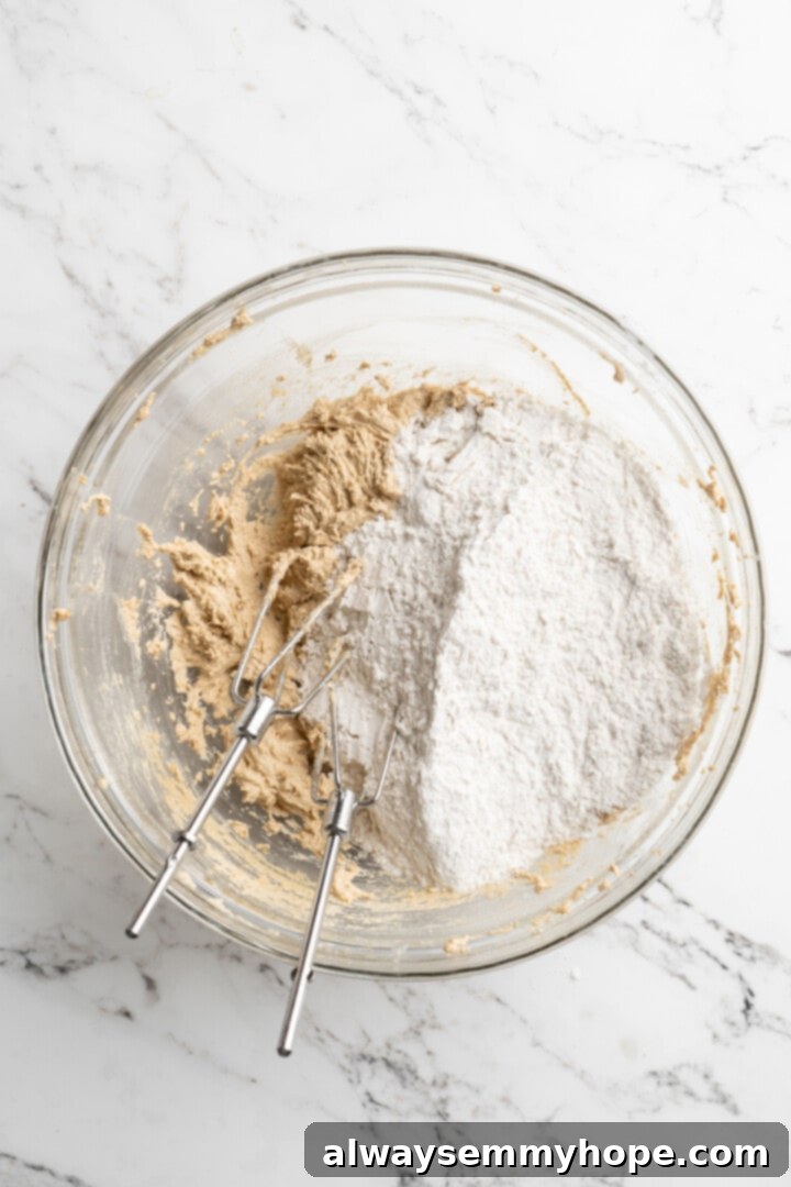 Thick, chewy, and loaded with chocolate, graham crackers, and marshmallows, this one-bowl s'mores cookie recipe is a guaranteed hit! Overhead view of dry ingredients for cookies (flour, cornstarch, baking soda, sea salt) being added to the bowl of wet ingredients.