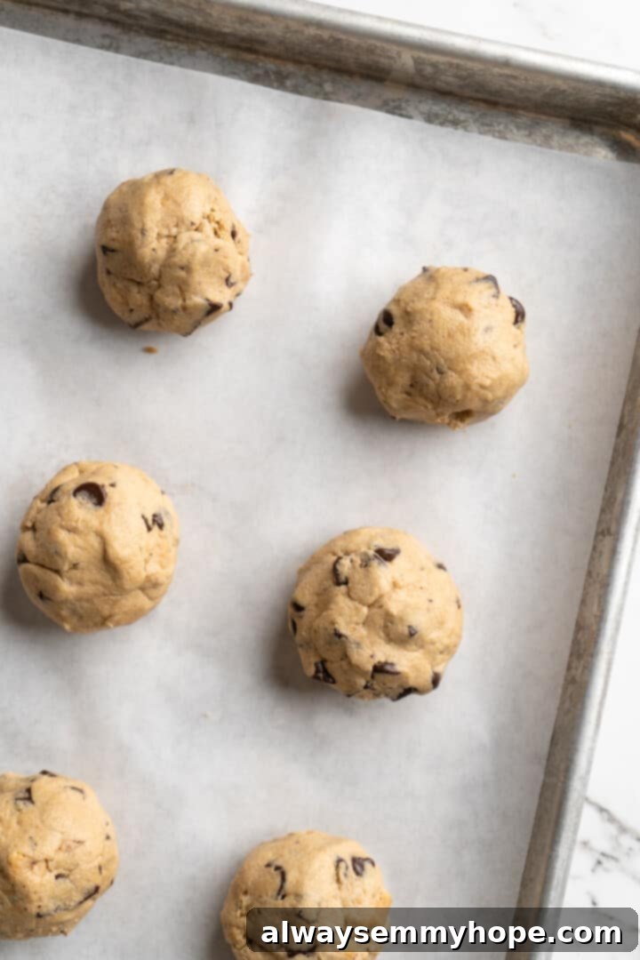 Thick, chewy, and loaded with chocolate, graham crackers, and marshmallows, this one-bowl s'mores cookie recipe is a guaranteed hit! Overhead view of perfectly portioned balls of s'mores cookie dough on a parchment-lined baking sheet before flattening.