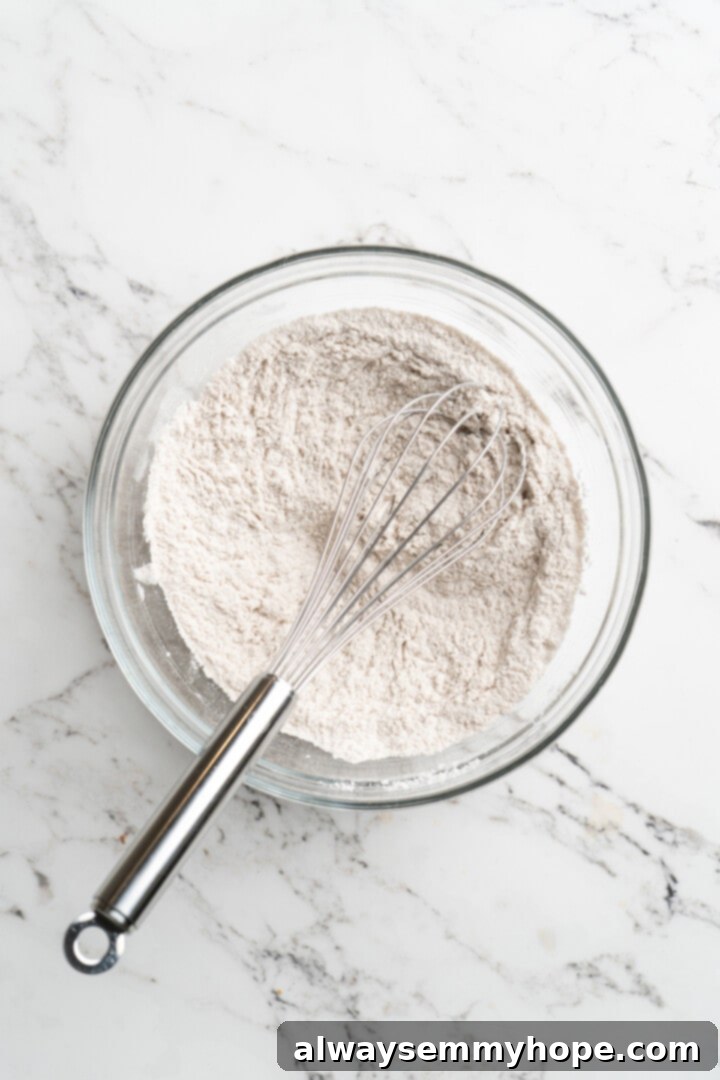 Overhead view of dry ingredients (flour, baking soda, cinnamon, salt) in mixing bowl with whisk