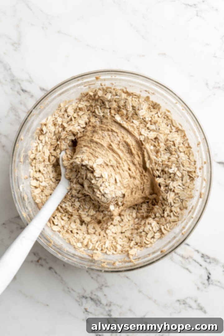 Overhead view of old-fashioned oats being gently folded into bowl of vegan cookie dough with a spatula